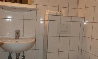 A simple bathroom with white tiles and basic equipment. There is a hand basin and a toilet.