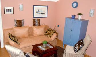 A cozy living room with a beige sofa and two chairs. Pictures hang on the wall, and a blue dresser is next to a small table.