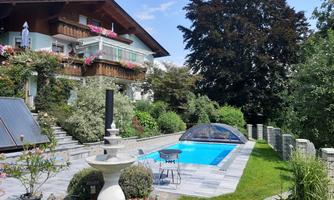 A beautiful garden with a pool and a terrace. The house has balconies with flower boxes and plenty of green vegetation.