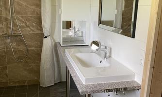 A modern bathroom with a shower and an elegant sink. The walls are brightly tiled, and there is a large window that provides plenty of light.
