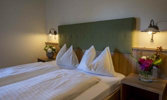 A cozy bedroom with a double bed and two large pillows. A table lamp and fresh flowers adorn the room.