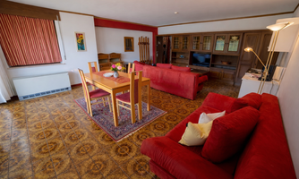 A spacious living room with red sofas and a dining table. In the background, a television and furniture can be seen.