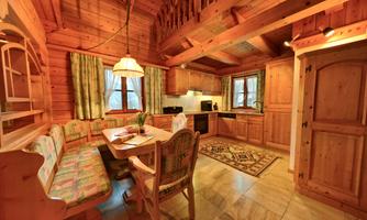 A cozy wooden kitchen with a seating area and a dining table. Large windows let in plenty of light and give the room a warm atmosphere.