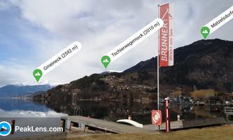 A serene lake with mountains in the background and a dock. In the foreground stands a sign with the inscription "BRUNNER".