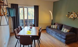 A modern living room with a dining area and a cozy sofa. Large windows provide plenty of light and a view outside.