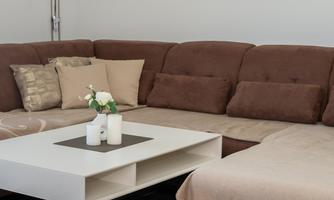 A modern living room with a brown couch and a white coffee table. The room has an elegant black floor and plenty of natural light.