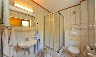 A bathroom with white tiles, shower, and sink. There are towels and a toilet.
