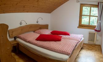 A cozy bedroom with a large wooden bed and red pillows. The window offers a view outside and lets in a lot of light.