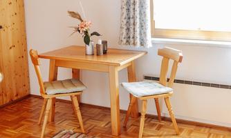 A small wooden tray with two chairs in a bright room. On the table, there is a vase with flowers and some decorative objects.