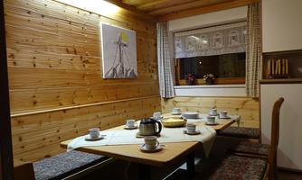 Interior view of a cozy vacation home with a large table set with cups and a teapot. The walls are made of wood, and there is a window with curtains and a beautiful view.