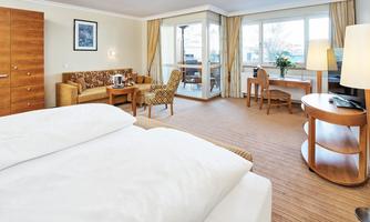 A modern hotel room with a cozy bed and a seating area. Large windows offer a beautiful view of the terrace and the outdoor area.