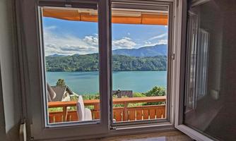 A beautiful view of a lake and the surrounding mountains through an open window. The sky is clear with some clouds.