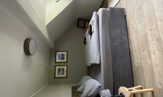 A cozy bedroom with a large bed and checked pillows. Two pictures are hanging on the wall, and the floor is made of wood.