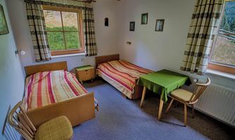 A simple room with two beds and a small table. The walls are painted light and there are windows with curtains.