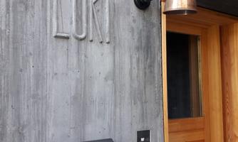 A modern entrance with a concrete wall and a wooden door. A copper lamp and a mailbox add a stylish touch to the design.