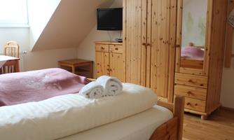 A cozy bedroom with wooden furniture and a television. Freshly folded towels and a blanket are lying on the bed.