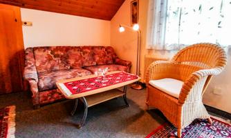 A cozy living room with a sofa and a wicker chair. The table has a red table runner and warm light from the floor lamp.