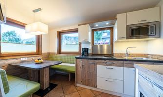 A bright kitchen with modern furniture and a cozy dining area. Large windows offer a view of the outdoors.
