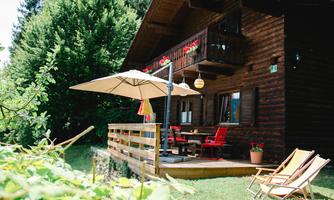 A cozy wooden house with a terrace and sunny garden. Red chairs and a sunshade invite you to relax.