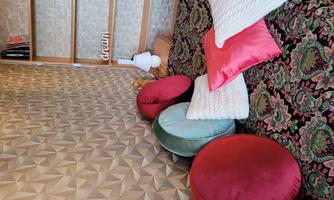 A cozy room with colorful cushions on a woven rug. In the background, there is a shelf with a lamp and the word "dream."