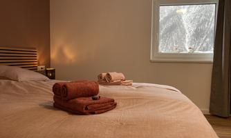 A cozy bedroom with a large bed and fresh towels. The view from the window shows snow-capped mountains.