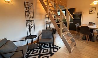 A cozy living space with modern furniture and a wooden staircase. The room is bright and friendly designed.