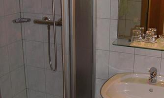 A simple bathroom with a shower and a sink. The walls are tiled with white tiles.