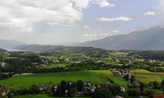 A vast, green landscape with gentle hills and a clear sky. In the foreground, small houses and fields are visible.