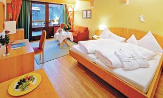 A cozy hotel room with a large bed and wooden furniture. There is a small table with fresh fruit and a seating area.