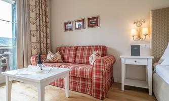 A comfortable living room with a checked sofa and a table. The walls are decorated and there is a balcony with a view outside.