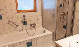 A modern bathroom with a bathtub and a shower. White tiles and wooden details create a bright, inviting atmosphere.