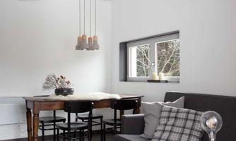 A modern furnished living room with a gray sofa and a large dining table. The decor is bright and open, featuring wooden details and a striped rug.
