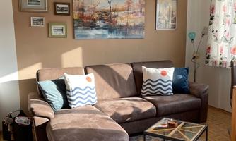 A cozy living room with a brown sofa and decorative pillows. Pictures hang on the wall and a rug lies on the floor.