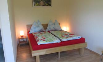 A cozy bedroom with a wooden bed and colorful bedspreads. Pictures hang on the walls, and there are two nightstands with lamps.