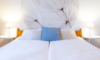A modern bedroom with two single beds. On the wall, there is a large decorative motif of a dandelion.