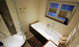A modern bathroom with a bathtub and a separate shower. There are bright walls and a large window with blinds.