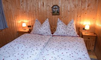 A cozy bedroom with a double bed and partly traditional pillows. The walls are made of wood and there is soft lighting next to the bed.