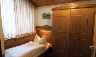 A simple bedroom with a single bed and wooden cabinets. The room has a window with curtains and a picture on the wall.