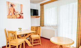 A cozy dining area with a wooden table and chairs. In the background, there is a window with curtains and a picture on the wall.