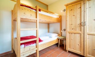 A cozy sleeping area with a wooden loft bed and a single bed. Next to the beds is a wooden wardrobe.