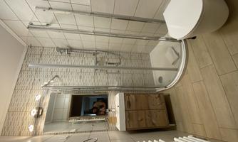 A modern bathroom with a glass shower and a sink. The walls are tiled and there is a towel radiator.