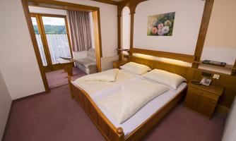 A cozy hotel room with a double bed and wood paneling. The room is bright and inviting, with an additional seating area and a window that leads to a balcony.