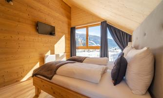 A cozy bedroom with wooden paneling and large windows. The room features a double bed and a television.