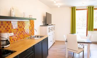 A modern kitchen with colorful tiles and wooden surfaces. The dining area is bright and inviting, with a large window and green curtains.