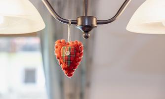 A red fabric heart hangs from a lamp. It has a checked pattern and a button in the middle.
