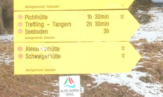 A yellow directional sign indicates various hiking destinations and their distances. There is information for hikers in the mountains.