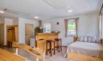 A bright and modern room with wooden furniture. There is a kitchen, chairs, and a cozy sleeping area.