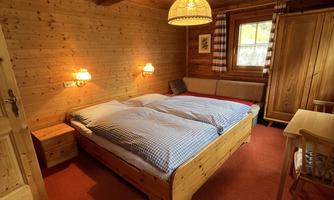 A cozy bedroom with a wooden ceiling and wood paneling. The room is equipped with a double bed, a desk, and a wardrobe.
