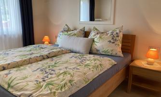 A cozy bedroom with a double bed and decorative pillows. Next to the bed are nightstands with soft lamps.