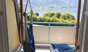 A cozy balcony with a rocking chair and a sun lounger. In the background, there is a beautiful view of the lake and the mountains.